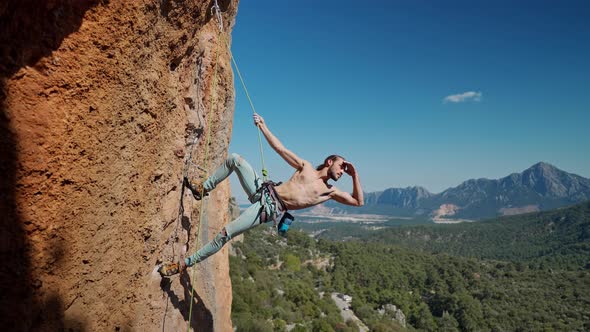 Strong and Muscular Fit Rock Climber Hangs on Rope on Vertical Cliff