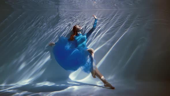 Attractive Young Woman Swims Beautifully Underwater in a Blue Dress Dress