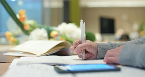 Woman study the note on paper with mobile phone at library 