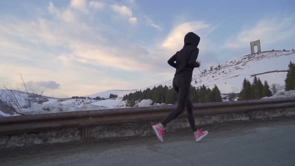 Young Fitness Woman Jogging in the Snow. Arc of Freedom in the Background with Colorful Clouds on