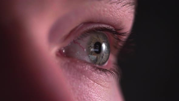 Reflection of screen on person's blue green eye in dark room 17