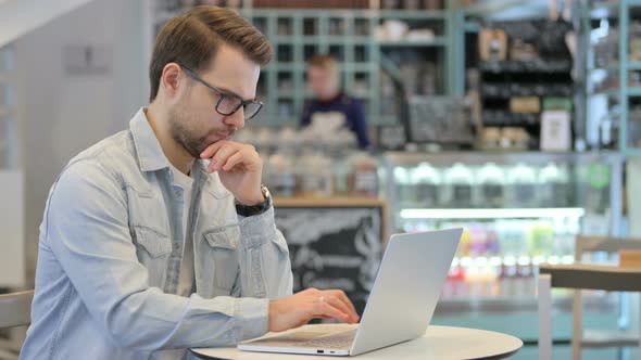 Man Thinking While Using Laptop in Cafe