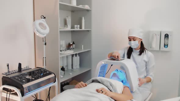 Woman Lying Under LED Light Facial Therapy Lamp in Beauty Salon