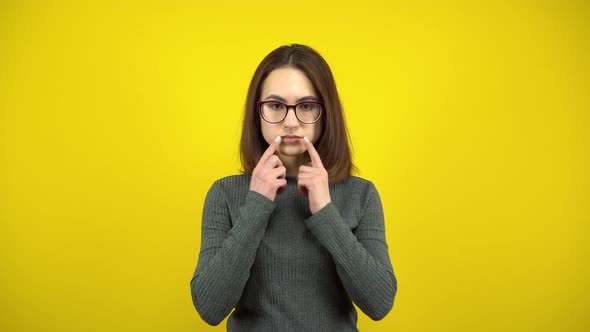 A Young Woman Makes a Cheerful Smile on Her Face with Her Fingers on a Yellow Background. Woman with