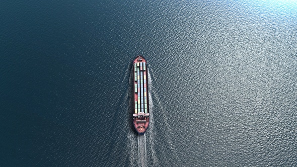 Airplane flies over Cargo ship  with containers in the sea- aerial