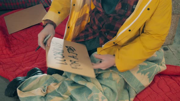 A Homeless Man is Writing on a Plate That He is Looking for a Job