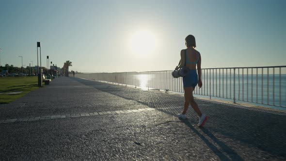 Sporty Young Athletic Girl with a Yoga Mat Walking Over a Bridge