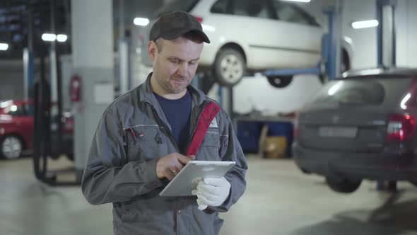 Confident Adult Caucasian Man Using Tablet and Showing Thumb Up at Camera in Car Repair Shop