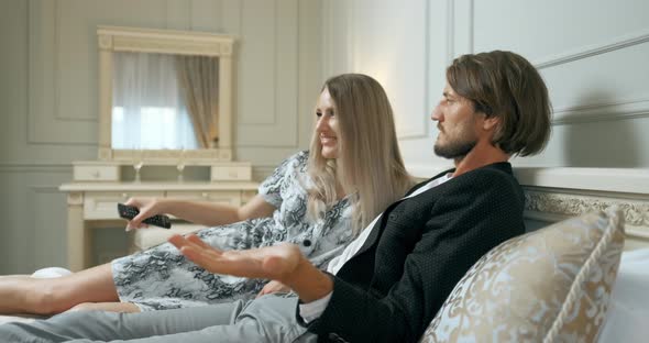 Happy Young Couple Is Lying on Bed and Watching TV at Home