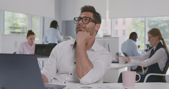 Inspired Indian Male Office Employee Looks Away Dreamily at Workplace