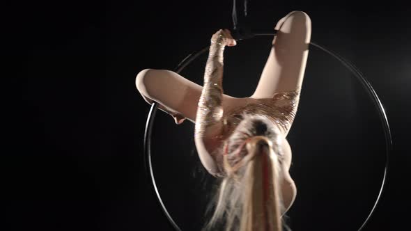 Portrait of Slim Young Woman Performing Acrobatic Tricks on Air Hoop at Black Background