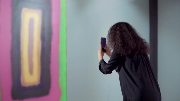 Brunette Woman Is Taking Photo of Abstract Picture in Exhibit Using Smartphone