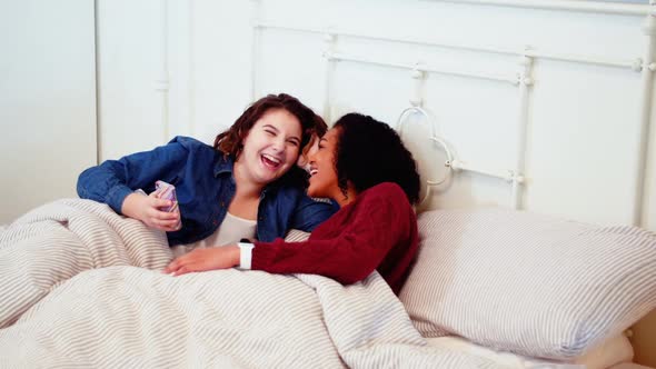 Lesbian couple using mobile phone on bed