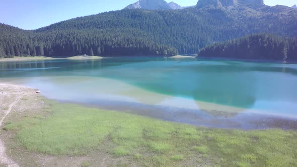 Clean, green, lake water with mountain tops and forest all around. Sunny, bright day.