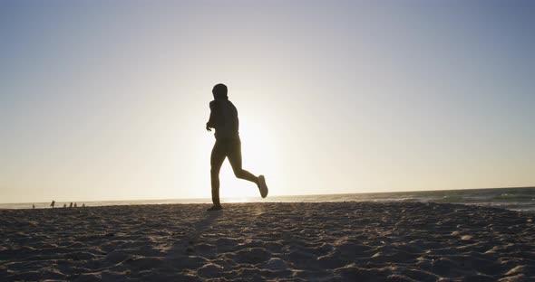 African american man running on beach, exercising outdoors in beach in the evening