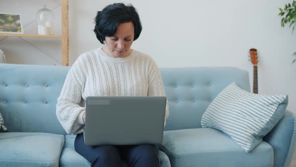 Mature Woman Using Laptop Typing Then Enjoying Good News Celebrating Success and Smiling at Home