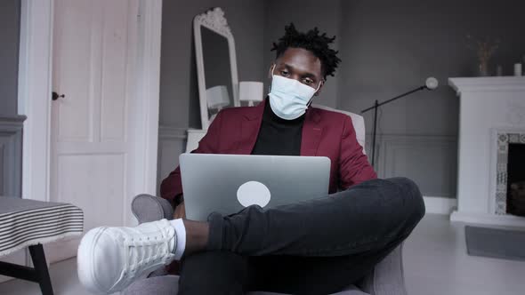 Black Business Man Works Behind a Laptop in a Protective Mask