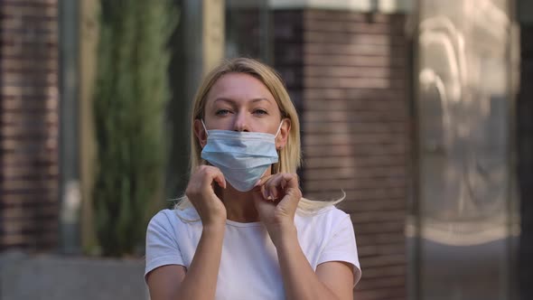 Portrait of Pretty Young Woman Looking Into the Camera and Putting on Medical Mask on Face for