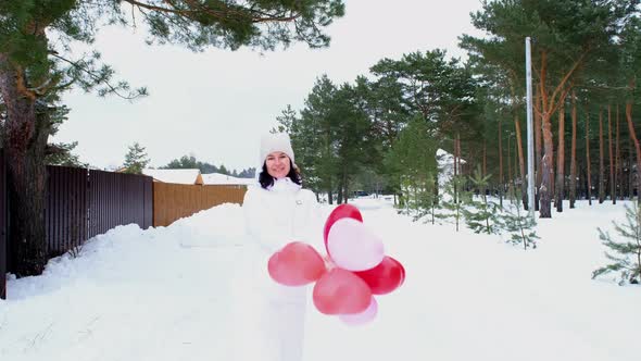 Happy woman throws up heart-shaped balloons outdoor in winter with snow