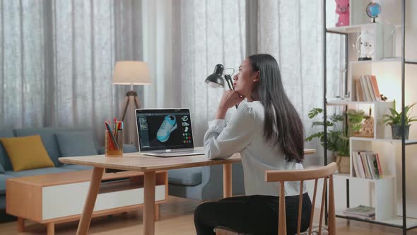 Asian Female Footwear Designer Thinking Then Raising Index Finger While Designing Shoe On A Laptop