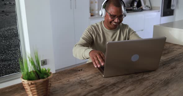 Senior african man doing video call with computer laptop while wearing headphones at home