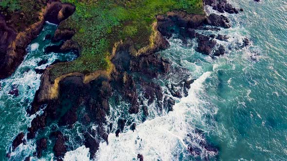 Waves crash against jagged rocky point on California coast at sunrise