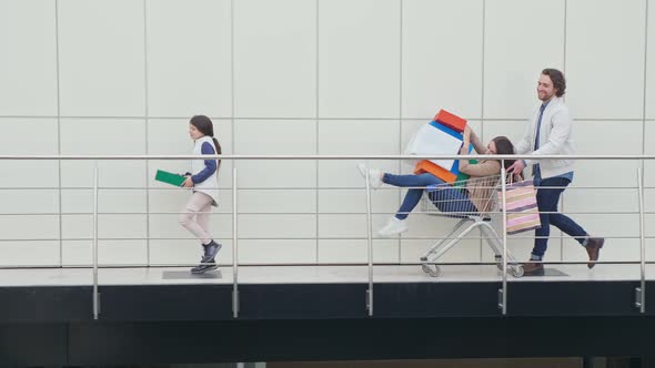 A Man Pushes a Shopping Cart With a Woman Holding Shopping Bags and Gifts for Christmas