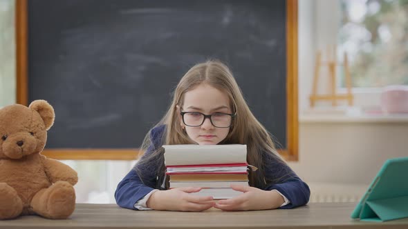 Portrait of Sad Teenage Girl Sitting in Classroom with Head on Books