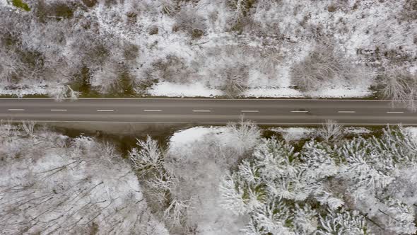 Winter country road with the view from above, fast driving cars passing by the straight street, top