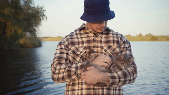 Young Guy Stroking a Cat on the Nature Near the Lake.