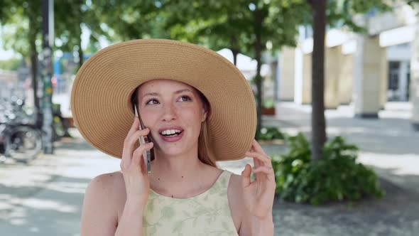 Young Pretty Woman Wearing Hat Walking on Summer City Street Taking on Phone