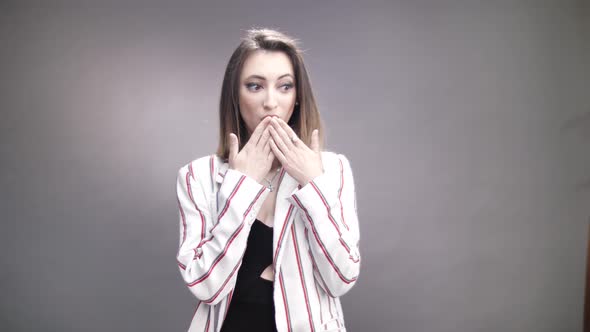Surprised petite woman covers her lips with hand on grey background