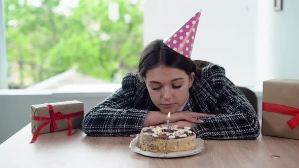 Sad Business Woman Celebrating Her Birthday Alone While Sitting in the Office Blows Out the Candle