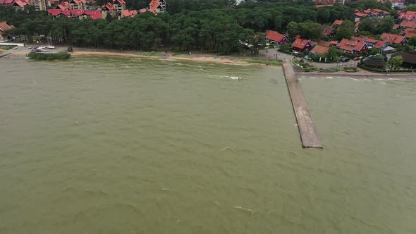 AERIAL: Wide Shot of Kite Surfer Jumping Over Stone Pier 