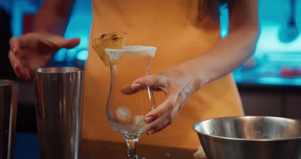 Close Up of Young Woman Hands Pouring Cocktail to Glass and Putting Pineapple