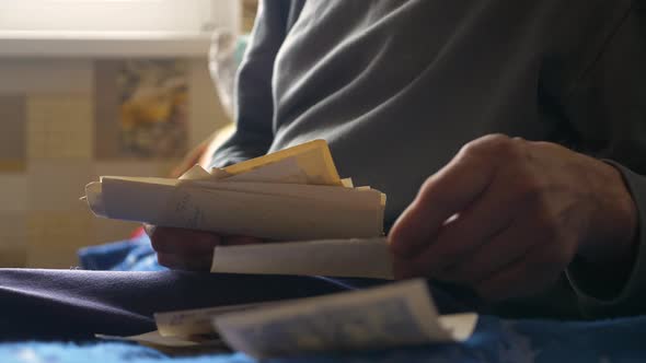 An aged man remembers and looks at old family photos holding them in his hands. Close-up in the hand