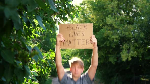 Young Teenager Male of Caucasian Ethnicity in Blue Shirt Holds Cardboard Box with Handwritten Text