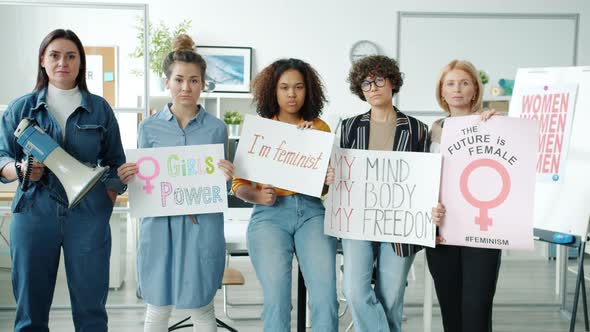 Group of Women with Feminist Posters Standing Indoors and Looking at Camera with Serious Faces