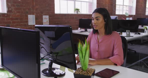 Mixed race businesswoman wearing headset sitting at desk having video call
