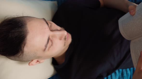 Man Thoughtfully Reading Book Comfortably Lying on Sofa