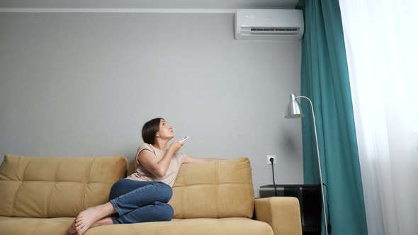 Woman Adjusts the Air Conditioner While Sitting on the Couch Slow Motion