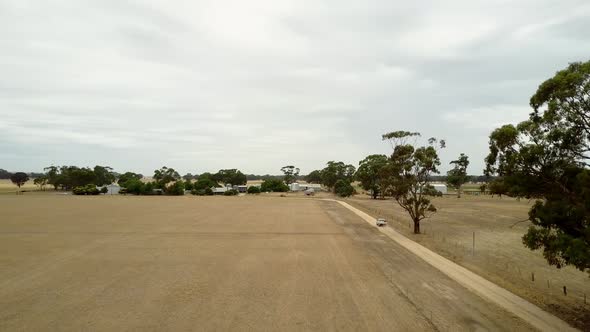 Establishing and follow shot of pickup truck driving on country dirt road towards farm yard.