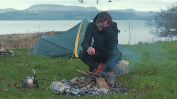 Camping young man puts kettle on fire camping by lake 4K