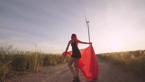 Woman with Pieces of Red Cloth Dance Near the Field with Wind Generators 