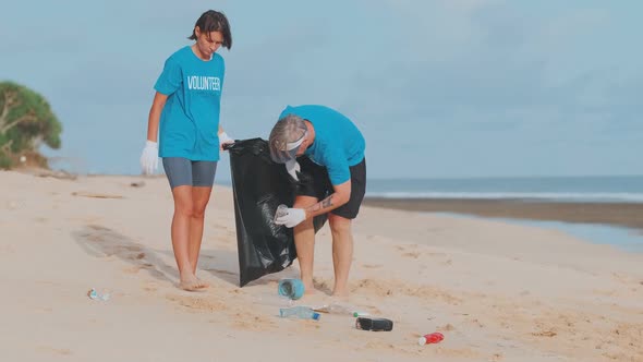 Young Caucasian Man and Woman Cleaning Up Plastic Garbage From Beach