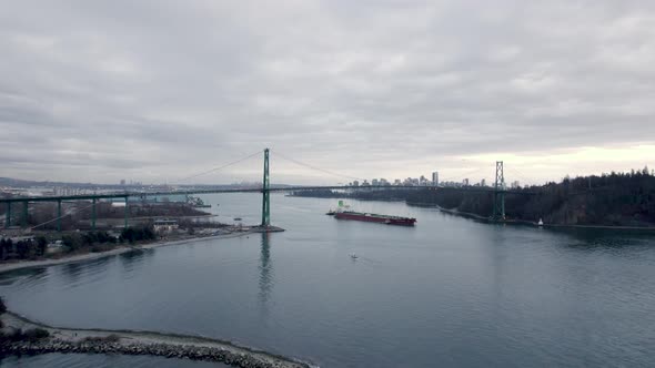 Barge passing under Lions Gate bridge with city and skyscrapers in background, Vancouver in Canada.