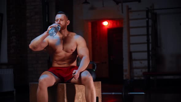 Strong Man Sitting in the Gym and Drinks Water From the Bottle