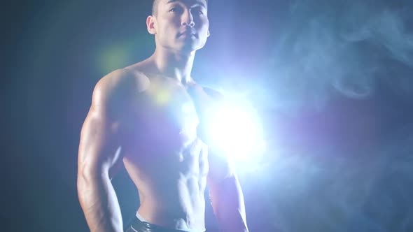 Asian Muscular Man Demonstrates His Body, Strength and Endurance. Black Smoke Background