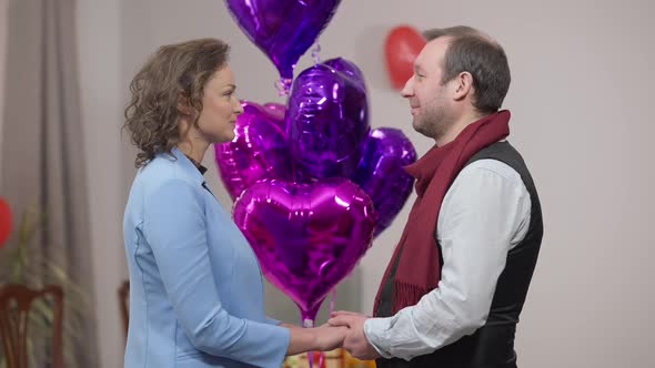 Smiling Loving Couple Looking at Each Other with Love and Kissing with Heart Shape Balloons at