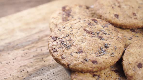 Sprinkling oatmeal chocolate chip cookies with poppy seeds in slow motion on a wooden background